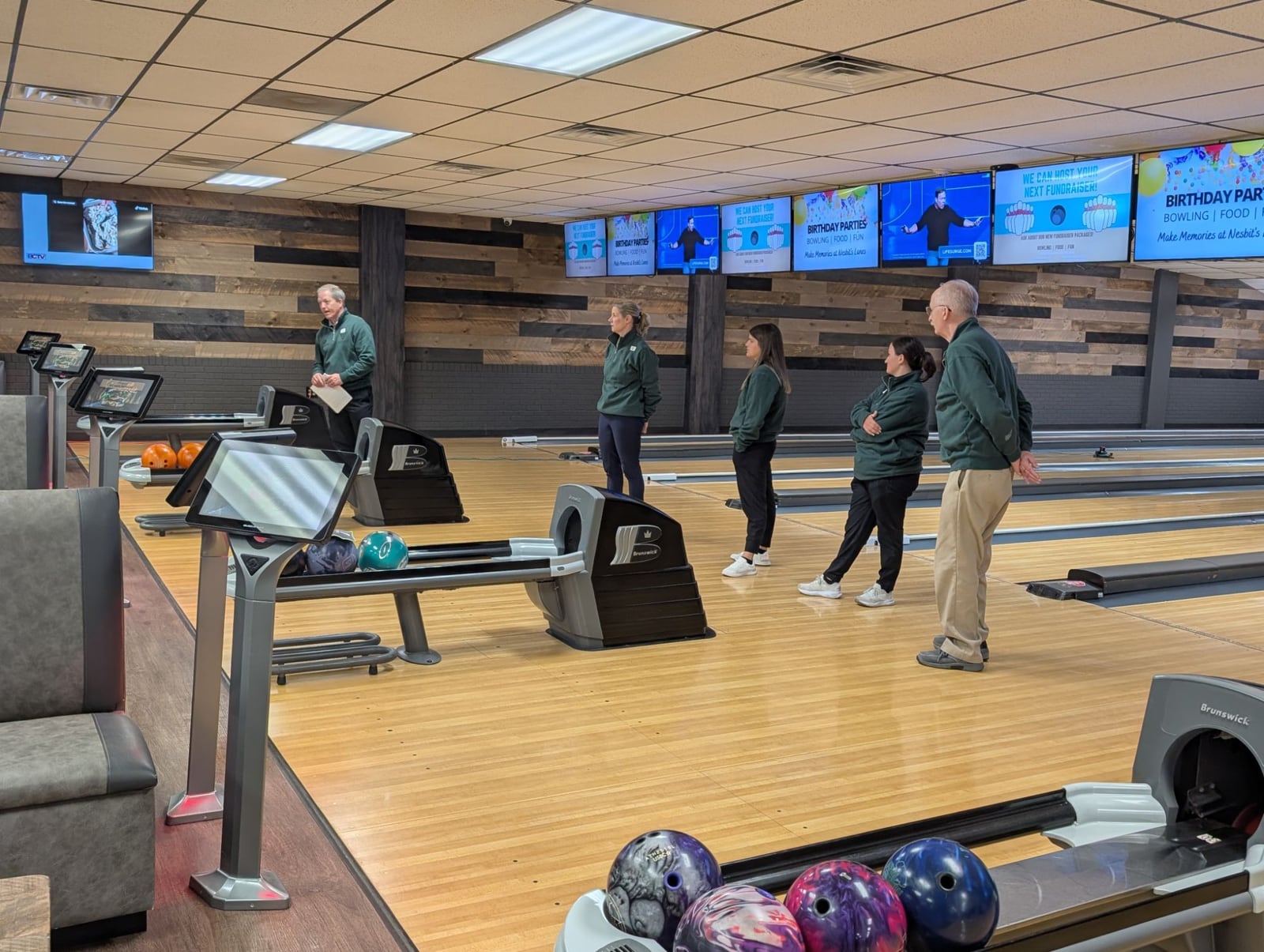 Mike Shady speaking on the lanes as four coaches in matching jackets listen